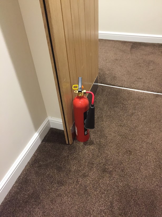 Fire extinguisher incorrectly used to prop open a fire door — a common fire safety compliance failure